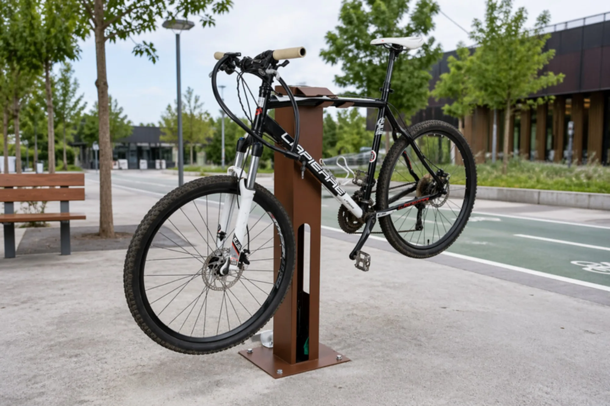 Station de réparation vélo en libre-service installée en espace public, à côté d'une piste cyclable, un VTT suspendu par le cadre