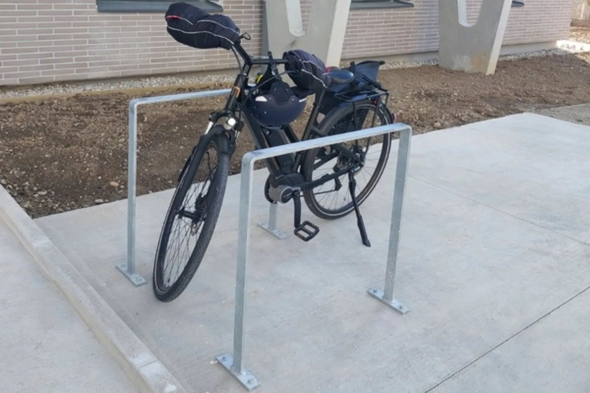 Arceaux vélo Recto en acier galvanisé fixés sur platines devant un bâtiment de campus, un vélo électrique attaché